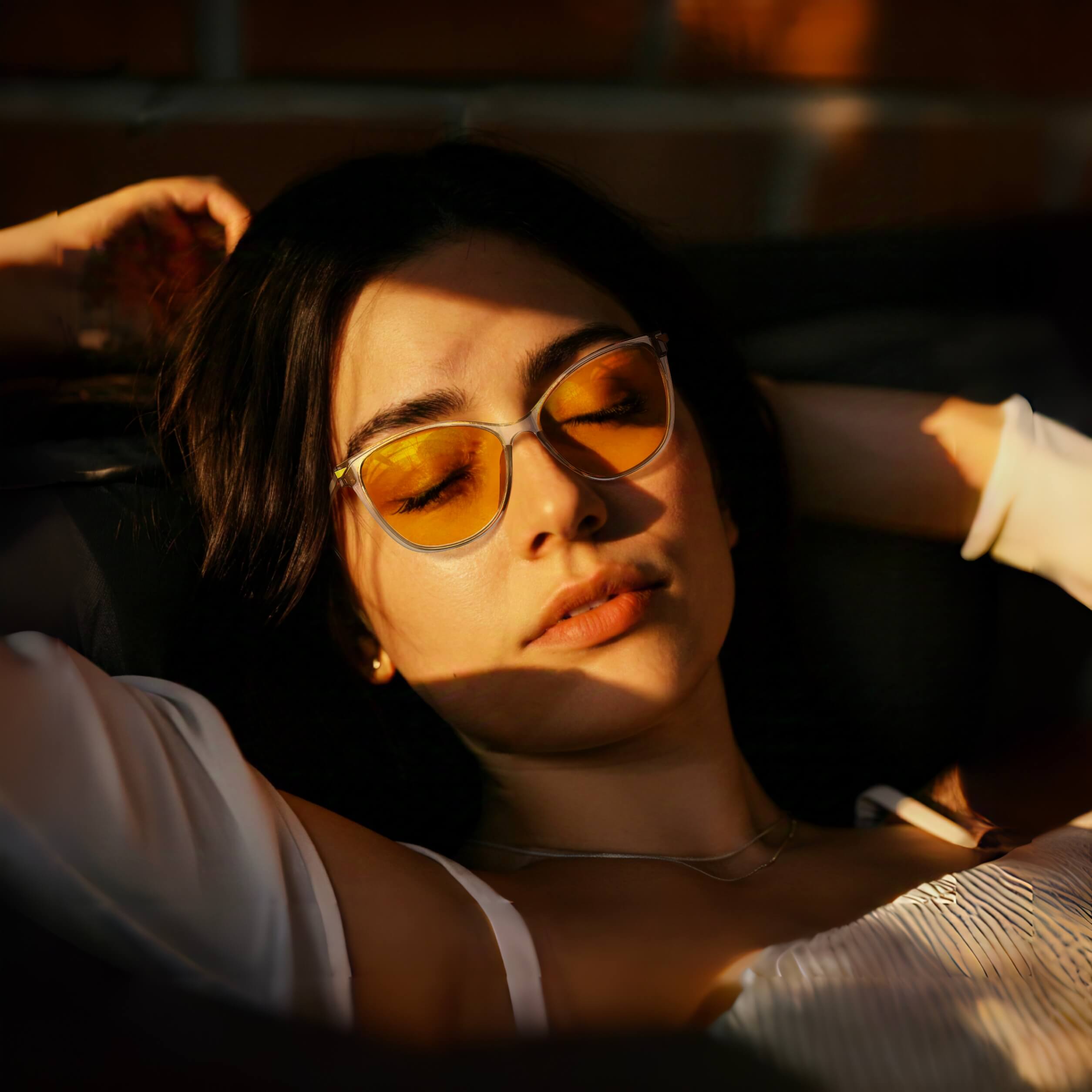 a young woman is wearing night ease cat eye sleep glasses with grey gold frame and sleeping putside under the sunlight