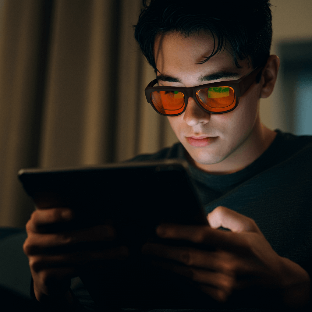 a boy is wearing night ease square fitover sleep glasses with black frame on his prescription glasses to blocking artificial light from tablets during digital time