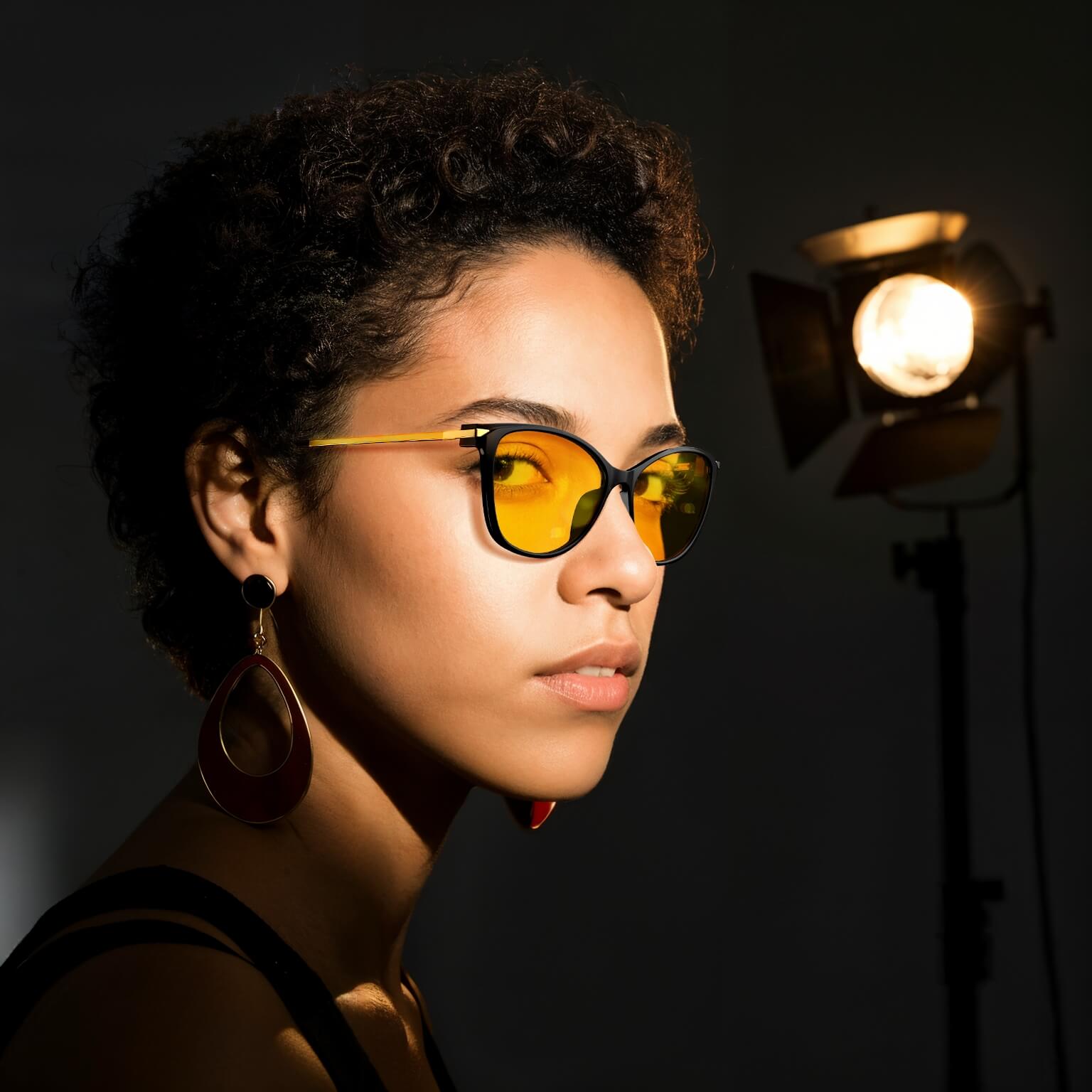 a fashion lady is wearing amber shield cat eye light sensitivity glasses with black frame for blocking artificial light like camera lighting