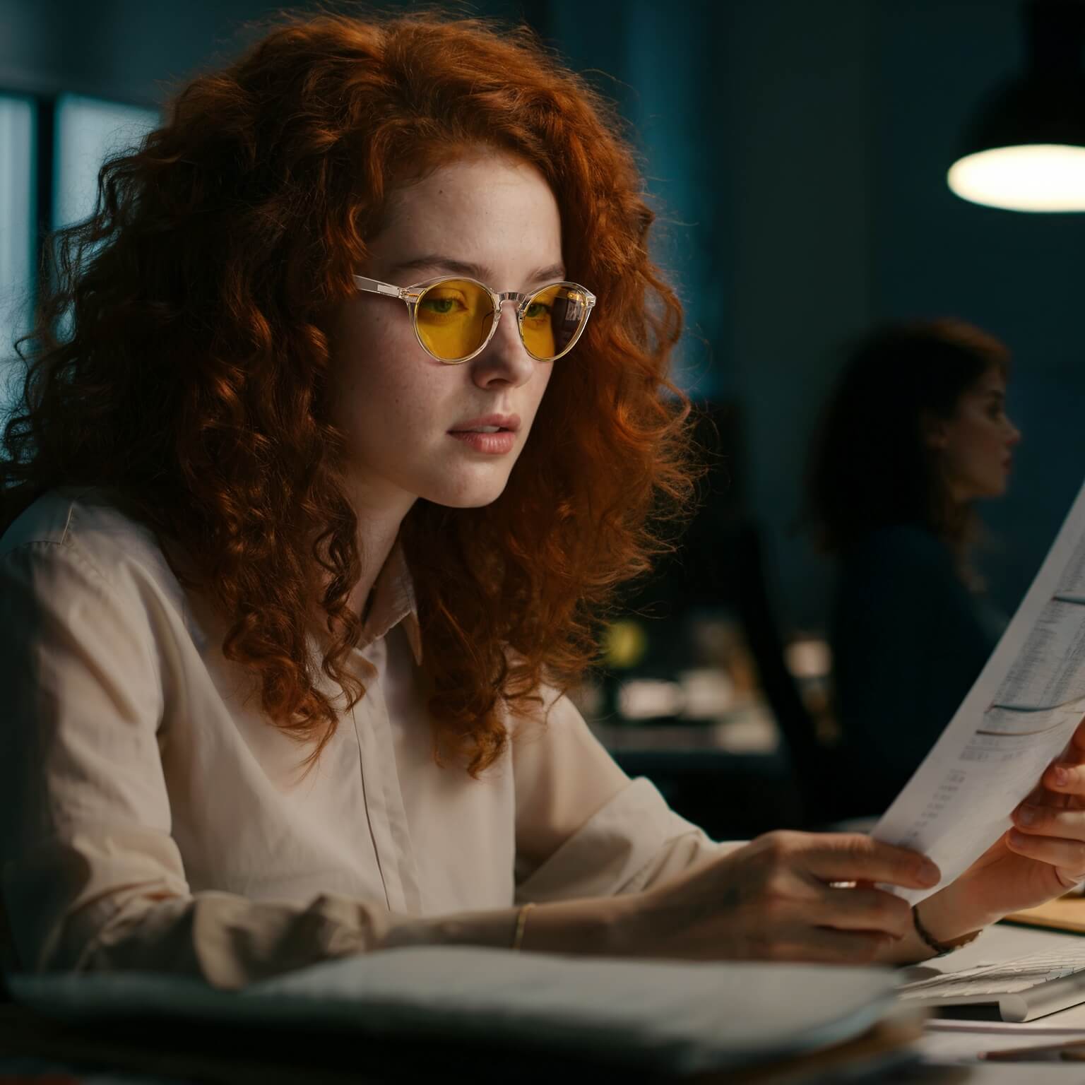 a young woman is wearing amber shield round light sensitivity glasses with clear frame for working during the day and night