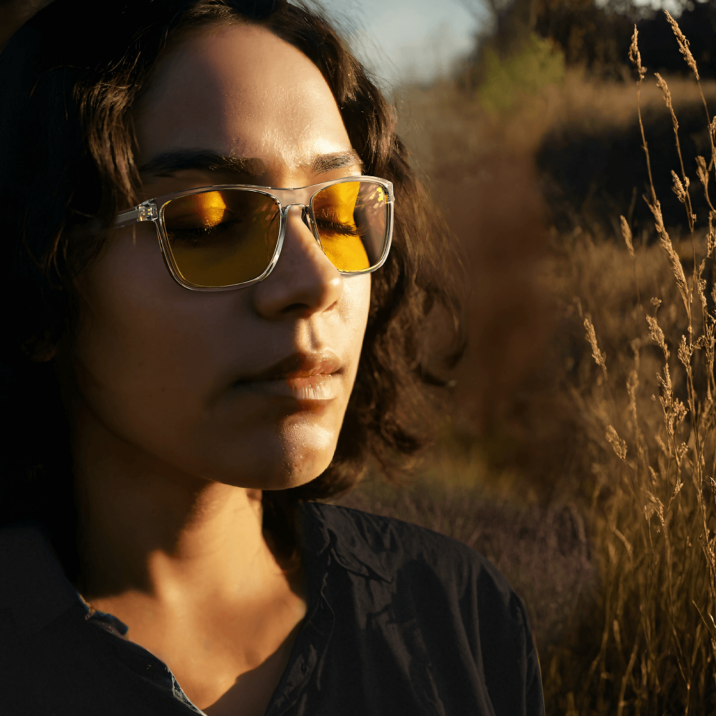 a young woman is wearing amber shield wayfarer light sensitivity glasses with clear frame for under sunlight