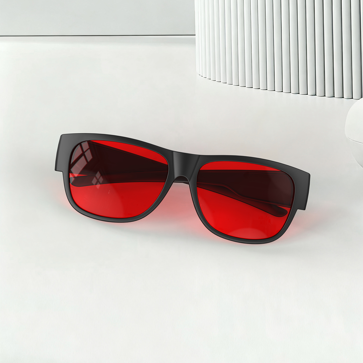 Night Ease™ Square Fitover red lens glasses for sleep placed on a clean surface, showing sleek frame design and vivid red anti-blue light lenses